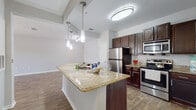This single-story residence is designed with an open, flowing layout that connects the kitchen, dining, and living areas seamlessly. The kitchen serves as a central focal point, showcasing a large island with granite countertops, an integrated sink, and stylish pendant lighting overhead. Dark espresso-toned cabinetry provides ample storage, complemented by a full suite of stainless steel appliances, including a refrigerator, electric range, built-in microwave, and dishwasher. A double-door pantry adds further storage convenience.

Wood-style flooring extends throughout the main living areas, lending warmth and visual continuity. The living room is generously proportioned, featuring a ceiling fan, a sliding glass door that fills the space with natural light, and direct access to an outdoor area. An additional room, suitable as a bedroom or flex space, benefits from multiple windows with exterior views and its own ceiling fan.

The bathroom is finished with wood-look tile flooring, a tiled tub and shower combination accented by a decorative border, a vanity with dark cabinetry, and brushed nickel fixtures. Neutral wall tones and clean white trim throughout contribute to a bright, cohesive aesthetic across the entire unit.
