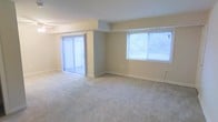 This two-floor residential space offers a functional and well-lit layout designed for comfortable everyday living. The main living area is generously proportioned, featuring plush wall-to-wall carpeting that adds warmth underfoot. Natural light flows freely into the space through a large sliding glass door fitted with vertical blinds, which provides direct access to an outdoor area, as well as a wide window that further brightens the interior. The neutral, light-toned walls create a clean and versatile backdrop suitable for a variety of furnishing styles. Subtle architectural detailing, including a structural beam element, adds a modest sense of definition to the open floor plan. The overall ambiance is bright and airy, with a simple, understated aesthetic. Spanning two floors, the space provides ample room for both living and private areas, offering a practical separation between communal and personal spaces. The combination of carpet flooring, abundant natural light, and outdoor access makes this a welcoming and livable environment well-suited for daily use.