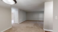 Located at 260 Northern Ave in Avondale Estates, Georgia, this 2-bedroom, 1-bathroom unit offers a functional single-floor layout designed for comfortable everyday living. The open living room features neutral gray walls, plush wall-to-wall carpeting, and a textured ceiling, with a pendant light fixture anchoring the entry area and a door leading outdoors for natural light. The kitchen is well-appointed with warm wood cabinetry, stone-patterned countertops, a double-basin sink beneath a window, and black appliances including a range, dishwasher, and refrigerator. Durable hardwood-style flooring runs through the kitchen area, complementing the cabinetry tones. The spacious primary bedroom features large windows that invite abundant natural light, a built-in closet with bifold doors, and soft carpeting underfoot. The second bedroom is equally well-lit, with a window offering outdoor views and the same neutral carpeted flooring. The shared bathroom is clean and straightforward, featuring a full tub-shower combination with white surround, chrome fixtures, and hardwood-style flooring. Throughout the unit, a consistent neutral color palette and clean finishes create a cohesive and move-in-ready environment.