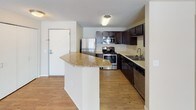 This single-floor residence offers a thoughtfully designed layout with two bedrooms, two bathrooms, and a versatile den. The kitchen serves as a functional centerpiece, featuring dark espresso cabinetry, stainless steel appliances including a refrigerator, range, microwave, and dishwasher, along with a granite-topped breakfast bar and hardwood-style flooring that creates a warm, inviting atmosphere. The open living area transitions seamlessly from the kitchen, featuring plush carpeting and a textured ceiling, providing ample room for comfortable living and entertaining. The primary bedroom is bathed in natural light through a bay-style arrangement of multiple windows with views of the surrounding landscape, complemented by soft carpeting throughout. The second bedroom offers a quiet, carpeted retreat with clean neutral walls. The den provides additional flexible space, also finished with carpet and neutral tones. The primary bathroom includes a granite-topped vanity and a tub-shower combination with white tile surround and tile flooring. The second bathroom features a tiled walk-in shower and clean tile flooring. Throughout the unit, neutral color palettes and consistent finishes create a cohesive, move-in-ready environment well-suited for a variety of lifestyles.