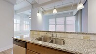 Located at 34 Sixth St W in Cincinnati, OH, this one-bedroom, one-bathroom unit offers a well-organized layout across a single floor. Light hardwood flooring runs throughout, lending warmth and visual continuity to the space.

The open kitchen is a standout feature, appointed with granite countertops, a subway tile backsplash, rich wood cabinetry, and a full suite of stainless steel appliances including a refrigerator, electric range, and microwave. A peninsula with pendant lighting above serves as a natural divide between the kitchen and the living area, providing additional counter and seating space.

The living room is generously proportioned, bathed in natural light from a bank of large windows fitted with roller shades. The bright, airy ambiance is further enhanced by the clean white walls and light flooring.

A hallway connects the main living areas to the bedroom, bathroom, two closets, and a utility room. The spacious primary bedroom features multiple windows that bring in ample natural light. The bathroom includes a full soaking tub with a textured surround wall. Two closets provide practical storage throughout the unit.

Exposed conduit and industrial-style track lighting on the ceiling add a subtle urban loft character to this efficiently designed downtown Cincinnati residence.