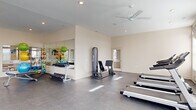 Located at 2335 N Cassady Ave in Columbus, Ohio, this fitness center offers a spacious, single-floor layout thoughtfully designed to support a full range of workout activities. The facility features durable, easy-to-maintain polished concrete flooring throughout, complemented by neutral-toned walls and recessed lighting that create a clean, energizing atmosphere.

The cardio zone is well-appointed with multiple treadmills and stationary bikes, each equipped with individual display screens for entertainment during workouts. Ceiling fans are strategically placed overhead to promote air circulation throughout the space. Wall-mounted televisions provide additional viewing options across the floor.

The strength training area includes a multi-function cable machine, a dedicated free weight rack stocked with dumbbells, and adjustable workout benches. A large wall mirror expands the sense of space and supports proper form during exercise. Colorful medicine balls and stability balls add versatile functional training options.

Large windows line multiple walls, allowing abundant natural light to fill the room while offering views of the surrounding exterior. The open floor plan provides ample room for stretching and bodyweight exercises, ensuring the space never feels crowded. An adjoining restroom or utility area is accessible from within the facility, adding convenience for users.
