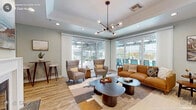 The Brookside Club House at 4849 Manzanita Ave in Carmichael, California is a thoughtfully designed single-floor community amenity space that blends modern aesthetics with comfortable, functional interiors. Guests are welcomed through a glass-paneled entryway featuring distinctive hexagonal tile flooring and soft sage-green walls, creating an inviting first impression accented by tasteful decorative touches.

The main lounge area is a standout feature of the club house, offering generous open space bathed in natural light from floor-to-ceiling sliding glass doors that open directly to the outdoor pool and pergola area. The room is furnished with mid-century modern pieces, including a warm cognac leather sofa, tufted accent chairs, and layered geometric rugs over light hardwood flooring. A sculptural globe chandelier serves as an elegant focal point overhead, complemented by recessed lighting throughout.

Additional seating areas provide intimate conversation nooks, each oriented toward the expansive outdoor views, reinforcing a seamless indoor-outdoor connection. A fireplace adds a cozy architectural element visible from the lounge.

The club house also includes a fully equipped galley-style kitchen outfitted with white cabinetry, granite-look countertops, stainless steel appliances, and hardwood-style flooring — ideal for community events and gatherings. Throughout the space, the consistent palette of soft blues, warm wood tones, and white trim creates a cohesive, welcoming atmosphere.