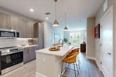 Located in Charlotte, NC, this thoughtfully designed one-bedroom, one-bathroom residence offers a efficient and well-appointed single-floor layout. Light wood-tone flooring flows throughout, tying together a cohesive modern aesthetic.

The open-concept kitchen is a standout feature, showcasing warm wood-grain cabinetry, a textured tile backsplash, stainless steel appliances including a range, microwave, and refrigerator, and a large center island with a white quartz countertop, undermount sink, and woven bar stools. Dual pendant lights in brushed brass add a refined finishing touch. The kitchen opens directly into the living room, which is bright and airy, benefiting from large windows that frame tree-lined outdoor views and allow generous natural light.

The bedroom is a calm, restful retreat featuring a ceiling fan, a well-sized window with outdoor views, and neutral wall tones that complement the light flooring. The bathroom is clean and contemporary, with a wood-toned vanity, white quartz countertop, and a full tub-shower combination tiled in classic white subway tile with brushed nickel fixtures.

Throughout the residence, neutral gray-toned walls, recessed lighting, and modern finishes create a polished, welcoming ambiance ideal for comfortable everyday living.