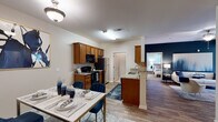 Located at 5418 Sirius Dr in Wilmington, NC, this single-floor residence offers a well-designed, open-concept layout that seamlessly connects the kitchen, dining, and living areas. The kitchen is equipped with warm-toned wood cabinetry, granite countertops, black appliances including a range, microwave, and refrigerator, and wood-look flooring that extends throughout the main living spaces. A peninsula with a sink adds functionality and serves as a natural divider between the kitchen and dining area, which is bright and inviting with a ceiling-mounted light fixture overhead. The living area is comfortable and airy, with neutral walls that complement the warm flooring. Bedrooms are carpeted for comfort, each featuring natural light from windows with blinds and sheer curtains. The primary bedroom includes access to a walk-in closet with wire shelving. The bathroom features granite countertops, a wood vanity, and an oversized mirror. Additional highlights include an in-unit laundry closet with stacked washer and dryer hookups, a dedicated water heater closet, and a bold accent wall in the living area that adds a modern design touch. The overall ambiance is clean, functional, and welcoming throughout.