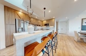 The Willow Penthouse in Hoboken, NJ is a sophisticated 1,410-square-foot residence featuring 3 bedrooms, 3 bathrooms, and 2 closets across a single floor. The open-concept kitchen is a standout, showcasing warm wood cabinetry, a marble-topped island with seating for four, a marble tile backsplash, stainless steel appliances, and gold fixtures—all set above light hardwood flooring that flows throughout the unit. The living and dining areas are bright and airy, anchored by floor-to-ceiling sliding glass doors that open to a private outdoor terrace with sweeping city views. The primary bedroom spans 210 square feet and features a clean, modern aesthetic with ample closet space. All three bedrooms are finished with light hardwood floors, neutral tones, and individual climate control units. The bathrooms are elegantly appointed with large-format tile, wood vanities, and brushed gold hardware; one features a glass-enclosed shower, while another includes a full soaking tub. Recessed lighting and large windows ensure natural light fills every room. The Willow Penthouse combines contemporary design with premium finishes, offering a refined urban living experience in one of Hoboken's most desirable addresses.