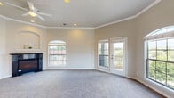 This single-floor residence offers a thoughtfully designed layout with a variety of functional and comfortable spaces. The expansive living room serves as the centerpiece of the home, featuring plush carpeting, elegant crown molding, a ceiling fan, a fireplace, and multiple arched windows that flood the room with natural light. A glass-paneled door opens directly to a private balcony, offering pleasant outdoor views of surrounding greenery and neighboring rooftops.

The bedrooms continue the warm, carpeted aesthetic and are accented with crown molding and ceiling fans. Arched windows provide additional natural light, creating bright and airy retreats. The bathrooms are finished with tile flooring, granite-topped wood vanities, and well-appointed fixtures. One bathroom features a curved glass-enclosed shower stall with tile surround, while another offers a dual-sink vanity with ample counter space.

The kitchen is outfitted with crisp white cabinetry, granite countertops, wood-look flooring, and black appliances including an electric range with overhead microwave and a refrigerator. The layout is efficient and well-organized, with generous cabinet storage throughout. Together, these spaces create a cohesive and comfortable living environment with classic architectural detailing and a neutral, inviting palette.