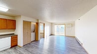 This single-floor residence offers a practical and comfortable layout with a variety of functional spaces throughout. The open living area is bright and inviting, featuring durable wood-look laminate flooring, a textured ceiling, and a sliding glass door that fills the room with natural light while providing access to an outdoor balcony with exterior views. Baseboard heating runs along the walls, ensuring warmth throughout the space.

The kitchen is well-equipped with warm oak cabinetry, dark countertops, and a full suite of white appliances including a refrigerator, electric range, microwave, and dishwasher. A skylight-style ceiling fixture provides ample overhead illumination, and the laminate flooring continues seamlessly from the adjoining living area.

An in-unit stacked washer and dryer is conveniently tucked behind a wood-paneled closet door, adding everyday practicality. The bedrooms are carpeted for comfort, each featuring windows with blinds that bring in natural light, and baseboard heaters to maintain a cozy atmosphere.

The bathroom is cleanly finished with oak vanity cabinetry, a granite-style countertop, a single-basin sink, a large mirror, and a full bathtub with a shower surround. Wood-look flooring ties the space together cohesively. Overall, the unit presents a clean, functional design with consistent warm wood tones throughout.