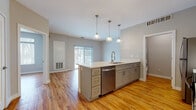 Located at 38601 Mentor Ave in Willoughby, Ohio, this single-floor residence offers a thoughtfully designed open-concept layout with a clean, contemporary aesthetic throughout. Warm honey-toned hardwood-style flooring flows seamlessly across every room, creating a cohesive and inviting atmosphere.

The kitchen is a standout feature, showcasing grey shaker-style cabinetry, white quartz countertops, and a full suite of stainless steel appliances including a refrigerator, range, and microwave. A central island with a built-in sink, dishwasher, and ample drawer storage doubles as a breakfast bar, illuminated by a trio of stylish pendant lights. White subway tile backsplash adds a classic touch to the galley-style cooking area.

The living area is bright and open, benefiting from a sliding glass door that invites natural light and provides outdoor views. A generously sized bedroom features a large multi-pane window overlooking wooded scenery and includes convenient access to a walk-in closet.

The bathroom is finished with elegant large-format tile in the walk-in shower, a white shaker vanity with quartz countertop, and consistent hardwood-style flooring. Neutral grey walls throughout the unit lend a modern, move-in-ready feel to this well-appointed Willoughby residence.
