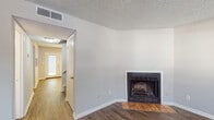 This two-floor residence offers a cohesive and functional layout finished with wood-style flooring that flows consistently throughout the home. The spacious living room serves as the heart of the main level, anchored by a classic fireplace with a tiled hearth and framed by neutral-toned walls and a textured ceiling. Natural light enters through blinds-fitted windows, enhancing the open, airy feel of the room. Adjacent to the living area is a dedicated dining space illuminated by an elegant chandelier and accessed via a pair of French doors that open to the outdoors, providing a seamless connection to the exterior. The galley-style kitchen is well-appointed with white shaker cabinetry, dark countertops, a double stainless steel sink, and black appliances including a refrigerator, dishwasher, and range. Multiple bathrooms are distributed across the two floors, each featuring wood-style flooring, white vanities, and clean, neutral finishes. The bedrooms are comfortable and well-lit, with ceiling fans for climate control and windows that bring in natural light. A staircase connects the two levels, and closet storage is present throughout. The home presents a clean, move-in-ready aesthetic with a neutral palette that suits a variety of interior styles.