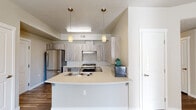Located at 2411 E Riverside Dr in Eagle, Idaho, this single-floor residence offers a clean, contemporary design with a cohesive neutral color palette throughout. The open-concept kitchen serves as the heart of the home, showcasing light wood-grain cabinetry, sleek light-colored countertops, and a suite of stainless steel appliances including a gas range, dishwasher, and refrigerator. A curved peninsula with an integrated sink and pendant lighting above provides additional prep space and casual seating. Wood-look flooring runs through the main living and kitchen areas, lending warmth and easy maintenance to the space. The bedrooms feature plush carpeting, natural light from windows with blinds, ceiling fans, and built-in closet storage, creating comfortable and functional retreats. The bathrooms are well-designed, with one featuring a tub-shower combination alongside a vanity with wood-grain cabinetry, and another outfitted with accessibility-friendly grab bars, a teak shower bench, and a walk-in shower — demonstrating thoughtful, inclusive design. The overall ambiance is bright, modern, and inviting, with consistent finishes and a practical layout that maximizes the efficiency of the single-floor plan.