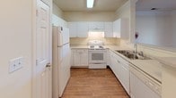 This single-story residence offers a thoughtfully designed layout with a seamless flow between its main living spaces. The kitchen is outfitted with white cabinetry extending to the upper walls, light countertops, white appliances including a refrigerator and electric range, and a double sink. Wood-look flooring runs throughout the kitchen, and a pass-through connects it to the living area, enhancing the open feel.

The living and dining area features warm hardwood-style flooring, crown molding, a ceiling fan, and a large window that draws in natural light. A fireplace serves as a focal point, adding character to the space.

The bedrooms are carpeted and generously sized, each benefiting from natural light through large windows with blinds. Walk-in closets provide ample storage, and one bedroom includes access to an additional adjoining room or closet space.

Both bathrooms feature wood-look flooring, full tub and shower combinations with decorative brown tile accents, white vanities with sinks, and mirrors. The neutral color palette throughout the residence creates a clean, cohesive aesthetic suited to a variety of furnishing styles.