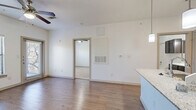 Located in Boerne, TX along Interstate 10 W, this one-bedroom, one-bathroom unit offers a well-organized single-floor layout designed for comfortable everyday living. The open-concept living and kitchen area is anchored by warm wood-look flooring that extends throughout the main space, creating a cohesive and inviting atmosphere. The kitchen is a standout feature, equipped with dark espresso cabinetry, black appliances including a refrigerator, range, and microwave, and a granite-topped island that doubles as a prep and dining surface. Pendant lighting above the island adds a stylish finishing touch, while the adjacent living area benefits from a ceiling fan overhead. The bedroom is generously proportioned, featuring plush carpeting, a ceiling fan, and a large window dressed with blinds that invites natural light and offers views of surrounding greenery. The bedroom connects directly to a dedicated closet and the full bathroom, which is finished with matching dark cabinetry, a white countertop vanity, light wood-look flooring, and a tiled shower-tub combination. Clean white walls throughout the unit lend a bright, neutral backdrop, making the space feel open and move-in ready. The efficient, functional layout makes excellent use of every square foot.