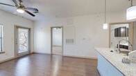 Located in Boerne, TX along Interstate 10 W, this one-bedroom, one-bathroom unit offers a well-organized single-floor layout designed for comfortable everyday living. The open-concept living and kitchen area is anchored by warm wood-look flooring that extends throughout the main space, creating a cohesive and inviting atmosphere. The kitchen is a standout feature, equipped with dark espresso cabinetry, black appliances including a refrigerator, range, and microwave, and a granite-topped island that doubles as a prep and dining surface. Pendant lighting above the island adds a stylish finishing touch, while the adjacent living area benefits from a ceiling fan overhead. The bedroom is generously proportioned, featuring plush carpeting, a ceiling fan, and a large window dressed with blinds that invites natural light and offers views of surrounding greenery. The bedroom connects directly to a dedicated closet and the full bathroom, which is finished with matching dark cabinetry, a white countertop vanity, light wood-look flooring, and a tiled shower-tub combination. Clean white walls throughout the unit lend a bright, neutral backdrop, making the space feel open and move-in ready. The efficient, functional layout makes excellent use of every square foot.