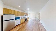 Located in Seattle, WA, this thoughtfully designed unit offers 1 bedroom and 2 bathrooms within a compact, efficiently laid-out single-floor plan. The open-concept kitchen and living area forms the heart of the space, featuring warm wood-tone cabinetry extending to the ceiling, stainless steel appliances including an electric range and dishwasher, a single-basin sink, and a window that draws in natural light. The kitchen flows seamlessly into the living area, where light wood-look flooring and crisp white walls create a bright, clean atmosphere throughout.

The bedroom is a well-proportioned, sun-filled room with two windows offering views of the surrounding neighborhood, allowing ample natural light to fill the space. A closet provides dedicated storage. The two bathrooms are finished in a modern, minimalist style — one features a bathtub with a wall-mounted towel rack, while the other offers a walk-in shower with a sleek surround, a toilet, and chrome shelving. Both maintain the consistent clean aesthetic found throughout the unit. Hallways connect the rooms with ease, contributing to a logical and functional flow. The warm flooring, recessed lighting, and neutral palette give the entire unit a cohesive, contemporary character.