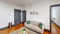 Located at 51 E Church St in Martinsville, Virginia, this one-bedroom, one-bathroom unit offers a well-organized and efficiently designed single-floor layout. The living room serves as the heart of the space, showcasing warm parquet wood flooring that adds a classic character throughout. Crisp white walls and recessed lighting keep the area feeling bright and open, while bold dark-painted doors provide a striking contrast. A window with blinds allows natural light to filter in, with views of the surrounding streetscape. The living area comfortably accommodates both a seating arrangement and a dining nook, making smart use of the available space. The bedroom features the same warm hardwood flooring, complemented by large windows fitted with horizontal blinds that invite natural light. A classic cast-iron radiator beneath the window speaks to the building's historic character. The bathroom is clean and functional, with a white vanity, a tiled hexagonal mosaic floor, and a shower-tub combination enclosed by a neutral curtain. Overall, the unit presents a tidy, well-maintained interior that blends historic architectural details with practical, modern living essentials.