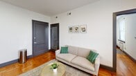 Located at 51 E Church St in Martinsville, Virginia, this one-bedroom, one-bathroom unit offers a well-organized and efficiently designed single-floor layout. The living room serves as the heart of the space, showcasing warm parquet wood flooring that adds a classic character throughout. Crisp white walls and recessed lighting keep the area feeling bright and open, while bold dark-painted doors provide a striking contrast. A window with blinds allows natural light to filter in, with views of the surrounding streetscape. The living area comfortably accommodates both a seating arrangement and a dining nook, making smart use of the available space. The bedroom features the same warm hardwood flooring, complemented by large windows fitted with horizontal blinds that invite natural light. A classic cast-iron radiator beneath the window speaks to the building's historic character. The bathroom is clean and functional, with a white vanity, a tiled hexagonal mosaic floor, and a shower-tub combination enclosed by a neutral curtain. Overall, the unit presents a tidy, well-maintained interior that blends historic architectural details with practical, modern living essentials.