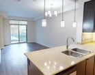 This 510-square-foot, single-floor, one-bedroom unit at 885-905 Southdale Road in London, Ontario, offers a practical and modern layout suited for individuals or couples. The open-concept living and kitchen area forms the heart of the unit, finished with durable wood-look laminate flooring throughout. The kitchen features dark espresso cabinetry extending to the ceiling, light-toned countertops, a double-basin sink set into a breakfast bar peninsula, stainless steel appliances including a refrigerator, electric range, and over-the-range microwave, and warm pendant lighting overhead. The kitchen floor transitions to light ceramic tile, providing a subtle distinction from the living area. The living room benefits from large sliding glass doors that open to a private balcony, allowing natural light and outdoor views of the surrounding neighbourhood. The 120-square-foot bedroom includes a double-door closet, wood-look flooring, and a large window providing additional natural light and exterior views. Neutral, cream-toned walls throughout the unit contribute to a clean, understated aesthetic.