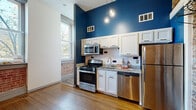 Located at 806 E Chestnut St in Louisville, KY, this one-bedroom, one-bathroom apartment blends historic character with modern updates throughout its efficiently designed layout. The open kitchen serves as a true centerpiece, boasting bold deep-blue accent walls that rise to impressively tall ceilings, white shaker cabinetry, granite countertops, a classic subway tile backsplash, and a full suite of stainless steel appliances including a gas range, built-in microwave, dishwasher, and refrigerator. Pendant lighting adds a warm, stylish touch overhead. Exposed brick walls carry through the space, paying homage to the building's historic roots, while warm hardwood flooring grounds the living and kitchen areas. The bedroom features natural light from a window framed by charming exposed brick detail, complemented by durable wood-look flooring and access to a dedicated closet with a hanging rod. The bathroom is clean and well-appointed, with marble-look tile covering both the floors and tub surround, oil-rubbed bronze fixtures, and a storage cabinet. Throughout the unit, thoughtful design details — from the original-style paneled doors to the industrial-chic exposed pipes — create a space rich in personality and historic Louisville charm.