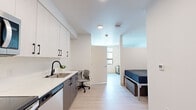 Located at 345 Lincoln Ave in Amherst, Massachusetts, this thoughtfully designed studio offers a smart, modern layout that maximizes every square foot across a single floor. Light wood-tone flooring and crisp white walls flow throughout the space, creating a clean, contemporary aesthetic.

The kitchen is a standout feature, outfitted with a full suite of stainless steel appliances — including a refrigerator, electric range, over-the-range microwave, and dishwasher. Two-tone cabinetry pairs white upper cabinets with warm wood-finish lower cabinets, complemented by white quartz countertops and a sleek black-accented sink. A built-in desk area provides a dedicated workspace within the main living area, while a bed nook with a window offers a defined sleeping zone.

The bathroom is finished in a consistent modern palette, featuring light wood-tone flooring, a wood-finish vanity with white countertop, a large mirror, and clean white walls with chrome fixtures. Ample wall space allows for practical towel storage.

A dedicated in-unit laundry room houses a full-size Whirlpool front-loading washer and dryer side by side, with overhead wire shelving for additional storage. This well-appointed studio combines efficient design with quality finishes throughout.