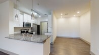 This single-floor residence offers a thoughtfully designed open-concept layout that seamlessly connects the kitchen and living area. The kitchen is a standout feature, equipped with stainless steel appliances including a range, over-the-range microwave, and refrigerator. Crisp white shaker-style cabinetry provides generous storage, while dark granite countertops add a refined contrast. A peninsula with a granite countertop and undermount sink extends into the living space, ideal for casual dining or entertaining. Track lighting and a pendant light illuminate the kitchen, complementing the recessed lighting found throughout. Durable wood-style flooring runs through the main living areas and bedrooms, providing a cohesive and easy-to-maintain aesthetic. The living area is spacious and bright, featuring a ceiling fan and clean white walls that create a neutral, versatile backdrop. Two well-sized bedrooms each include ceiling fans and windows with blinds that allow for natural light. The full bathroom features a tub-shower combo, granite-topped vanity, tile flooring, and brushed nickel fixtures. A dedicated laundry area accommodates a full-size top-loading washer and includes overhead wire shelving for additional storage.
