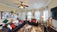 This two-story home offers a thoughtfully designed layout across multiple living spaces. The kitchen is a standout feature, boasting dark espresso cabinetry, light granite-style countertops, a subway tile backsplash, black appliances, and recessed lighting with pendant accents. A pass-through counter connects the kitchen to the adjacent dining area, which features hardwood-style flooring, a chandelier, and natural light from large windows with blinds. The living room is warm and inviting, highlighted by crown molding, a ceiling fan, and dual windows dressed with curtain panels that fill the space with natural light. An in-unit laundry closet provides convenient side-by-side washer and dryer hookups with overhead shelving. The bedrooms are carpeted and generously sized, each equipped with a ceiling fan and ample closet space. One bedroom includes direct access to an en-suite bathroom, which features wood-style flooring, a vanity with a large mirror, and a tub-shower combination. Throughout the home, warm neutral wall tones, crown molding details, and consistent finishes create a cohesive and comfortable living environment across both floors.