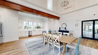 Located at 375 E Main St in Branford, CT, this single-floor space showcases a refined coastal farmhouse aesthetic defined by crisp white shiplap walls, warm hardwood flooring, and striking rich-toned wood beam accents that draw the eye upward toward impressively tall ceilings. The open-concept layout seamlessly connects the main living, dining, and kitchen areas, creating a cohesive and inviting environment throughout.

The living area is anchored by a classic fireplace with stone surround and is bathed in natural light from generously sized windows. Thoughtful touches such as a large statement wall clock and curated seating arrangements add character and comfort to the space.

The dining area sits beneath a bold wood beam and an elegant geometric chandelier, with a farmhouse-style dining table as its centerpiece, comfortably accommodating gatherings of various sizes.

The kitchen is outfitted with white shaker cabinetry, sleek white countertops, stainless steel appliances including a French door refrigerator and dishwasher, and a single-basin sink positioned beneath a multi-pane window that fills the space with natural light and views of the surrounding neighborhood.

Throughout, the consistent use of white shiplap, light hardwood flooring, and warm wood accents creates a unified, airy ambiance that is both stylish and welcoming.