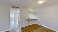 This single-story residence offers a practical and comfortable layout designed for everyday living. The main living area features warm hardwood flooring and a ceiling fan, with a sliding glass door that invites natural light and provides access to the outdoors. The open kitchen is a functional highlight, equipped with white cabinetry, a stone tile backsplash, black appliances including a refrigerator and range, and a generous butcher block breakfast bar that seamlessly connects the kitchen to the living space — ideal for casual dining or meal prep. A hallway leads from the main living area to the private quarters of the home. The bedrooms are carpeted for comfort and each features a ceiling fan with light fixture. The primary bedroom includes direct access to an en-suite bathroom and is complemented by a double-door closet offering ample storage. Additional closets provide further storage throughout. The bathrooms feature white square-tiled tub and shower surrounds with grab bars, offering clean and functional design. Textured ceilings are consistent throughout the home, adding a classic residential character. Overall, the space presents a straightforward, well-organized floor plan with a neutral color palette that creates a clean and move-in ready environment.