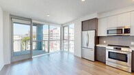 Located at 800 S Western Ave in Los Angeles, this modern unit offers a thoughtfully designed single-floor layout that maximizes both functionality and style. The open-plan living area is anchored by warm hardwood flooring and crisp white walls, creating a clean, contemporary ambiance throughout. Expansive floor-to-ceiling windows and a sliding glass door to a private balcony flood the space with natural light while framing sweeping views of the surrounding Los Angeles cityscape.

The kitchen is well-appointed with a full suite of stainless steel appliances, including a refrigerator, range, microwave, and dishwasher. Cabinetry combines dark wood lower units with white upper cabinets, complemented by light countertops and a tile backsplash, delivering a sleek, modern aesthetic. A dedicated in-unit laundry closet features a stacked washer and dryer, adding everyday convenience.

The bathroom is finished with large-format marble-look tile flooring, a tub and shower combination with full tile surround, and a wood-toned vanity, lending a clean and polished feel. A walk-in closet provides generous storage. The overall design reflects a modern urban sensibility, well-suited for city living in the heart of Los Angeles.
