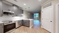 Located at 5672 Peachtree Pkwy in Peachtree Corners, GA, this thoughtfully designed single-floor unit offers a cohesive blend of modern aesthetics and functional living. The open-concept layout seamlessly connects the kitchen and living area, creating an inviting and efficient use of space.

The kitchen is a standout feature, showcasing gray shaker-style cabinetry with matte black hardware, white quartz countertops, a clean subway tile backsplash, and a full suite of stainless steel appliances including a refrigerator with ice maker, range, built-in microwave, and dishwasher. Stylish pendant lights hang above the peninsula, adding warmth and character. Light wood-look flooring runs throughout the main living areas, complementing the neutral color palette.

The living area opens directly onto a private balcony through sliding glass doors, allowing natural light to pour in and providing outdoor views of the surrounding community. Crown molding adds an elegant finishing touch to the main living space.

The bedroom is carpeted for comfort, features a ceiling fan, and includes a walk-in closet with built-in shelving and hanging rods for ample storage. A natural light source via a window overlooks the exterior.

The bathroom is finished with gray cabinetry, white countertops, matte black fixtures, and a full tub-shower combination with white tile surround, maintaining the unit's consistent modern design language.