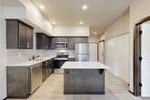 Located in Arlington, WA, this well-appointed one-bedroom, one-bathroom residence offers a thoughtfully designed single-floor layout that maximizes both function and comfort. The heart of the home is an open-concept living, dining, and kitchen area bathed in recessed lighting. The kitchen is a standout, showcasing dark espresso cabinetry with sleek hardware, a light-toned quartz countertop, a subway tile backsplash, stainless steel appliances — including a range, microwave, dishwasher, and refrigerator — and a central island with bar seating. Light wood-look flooring runs throughout the main living areas, lending a clean, modern aesthetic. A sliding barn door adds a stylish architectural accent. The bedroom features plush carpet flooring and a window that allows natural light to filter in, while a generous walk-in closet with wire shelving provides ample storage. A flexible den offers additional space suitable for a home office or hobby room. The combined bathroom and laundry room is efficiently designed, housing a stacked washer and dryer alongside a dark-cabinetry vanity. Three total closets ensure excellent storage throughout. The entrance hallway flows smoothly into the open living space, creating a welcoming and cohesive feel from the moment you step inside.