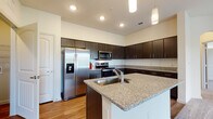 This well-designed single-floor residence offers a cohesive blend of modern finishes and functional living spaces. The kitchen serves as a central highlight, showcasing rich dark espresso cabinetry that extends to the ceiling for ample storage, granite countertops, and a full suite of stainless steel appliances including a side-by-side refrigerator with ice maker, a gas range, and an over-the-range microwave. A central island with an integrated sink and matching granite surface provides additional prep space and casual dining potential. Warm wood-look flooring flows throughout the kitchen and connecting areas, complemented by recessed lighting and elegant pendant fixtures overhead. A crisp white tile backsplash adds a clean, contemporary contrast to the dark cabinetry. The bedrooms are generously sized, finished with plush neutral carpeting and featuring large windows that allow natural light to fill the rooms. One bedroom includes a ceiling fan and a sliding closet, while another offers an arched doorway entry for added architectural character. The bathroom continues the home's design language with matching dark cabinetry, granite countertops, a large framed mirror, and wood-look flooring. Overall, the residence presents a clean, move-in-ready aesthetic with consistent, quality finishes throughout.