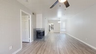 Located at 10455 E Via Linda in Scottsdale, Arizona, this single-floor residence offers a clean, modern aesthetic with a neutral color palette and light wood-look flooring carried consistently throughout. The open living area is a standout feature, anchored by a striking tile-surround fireplace that adds warmth and visual interest to the space. A ceiling fan overhead and natural light filtering through window blinds contribute to a comfortable, airy atmosphere. The living space flows seamlessly toward the kitchen and dining area, where a pendant light fixture provides focused illumination. The kitchen is appointed with white shaker-style cabinetry, light stone-look countertops, and stainless steel appliances including a range, over-the-range microwave, and refrigerator. The bedrooms are well-proportioned, each featuring ceiling fans, wood-look flooring, and windows that bring in natural light. The bathrooms are finished with matching white cabinetry, stone-look countertops, brushed nickel hardware, and a clean, minimalist design. The overall layout, as seen in the dollhouse view, is thoughtfully organized with clear separation between living, sleeping, and utility areas, making this Scottsdale residence both functional and visually cohesive.
