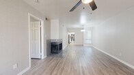 Located at 10455 E Via Linda in Scottsdale, Arizona, this single-floor residence offers a clean, modern aesthetic with a neutral color palette and light wood-look flooring carried consistently throughout. The open living area is a standout feature, anchored by a striking tile-surround fireplace that adds warmth and visual interest to the space. A ceiling fan overhead and natural light filtering through window blinds contribute to a comfortable, airy atmosphere. The living space flows seamlessly toward the kitchen and dining area, where a pendant light fixture provides focused illumination. The kitchen is appointed with white shaker-style cabinetry, light stone-look countertops, and stainless steel appliances including a range, over-the-range microwave, and refrigerator. The bedrooms are well-proportioned, each featuring ceiling fans, wood-look flooring, and windows that bring in natural light. The bathrooms are finished with matching white cabinetry, stone-look countertops, brushed nickel hardware, and a clean, minimalist design. The overall layout, as seen in the dollhouse view, is thoughtfully organized with clear separation between living, sleeping, and utility areas, making this Scottsdale residence both functional and visually cohesive.