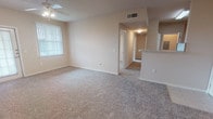 This single-floor unit offers a practical and comfortable layout designed to maximize functionality across two bedrooms and one bathroom. The living area is generously sized, finished with neutral-toned carpet and equipped with a ceiling fan. Vertical blinds dress the windows, and a glass-paned door provides additional access, likely to a patio or exterior space. A half-wall partition separates the living area from the kitchen, creating an open yet defined flow between spaces.

The kitchen features warm wood-toned cabinetry in a U-shaped configuration, offering ample storage and counter space. White appliances include a refrigerator, electric range, built-in microwave, and dishwasher, all set above light ceramic tile flooring.

Both bedrooms are carpeted and include ceiling fans with light fixtures. One bedroom features a built-in desk with overhead cabinetry, adding a functional workspace. A spacious walk-in closet with multiple wire shelving units provides generous storage. The second bedroom is well-proportioned with a large window allowing natural light.

The bathroom includes a tiled shower stall with accessibility grab bars, a toilet, and a vanity with storage. The overall aesthetic is clean, neutral, and move-in ready.