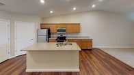 Located at 410 S Noyer Rd in Fort Wayne, Indiana, this single-floor residence offers a well-designed, functional layout with consistent finishes throughout. The kitchen serves as a central highlight, featuring warm honey-toned cabinetry, granite-look countertops, stainless steel appliances including a refrigerator, electric range, and built-in microwave, and a large island with a built-in sink. Rich wood-look flooring grounds the kitchen and flows into adjacent areas, complemented by recessed lighting overhead.

The bedrooms are generously sized, finished with neutral-toned carpet and warm beige walls that create a calm, understated ambiance. Each bedroom benefits from natural light through window treatments, and ceiling fans are present for added comfort. Sliding glass doors in one room open to outdoor views of the surrounding greenery.

The home includes two full bathrooms, both appointed with wood-look flooring, granite-look countertops, and warm wood cabinetry. The primary bathroom features a walk-in shower with built-in shelving, while the secondary bathroom offers a shower-tub combo. Both bathrooms are clean and practical in their design. Overall, the space presents a cohesive, move-in-ready interior with a neutral palette throughout.