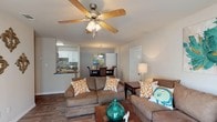 Located at 14510 Lemoyne Blvd in Biloxi, Mississippi, this single-floor residence features a cohesive coastal-inspired design throughout its well-appointed layout. The open living area serves as the heart of the home, finished with wood-style flooring and ceiling fans with light kits. Neutral wall tones provide a calm backdrop that complements the coastal decor accents found throughout the space. The living room flows naturally into the dedicated dining area, which is anchored by a pendant light fixture overhead and offers ample room for a full dining set. The galley-style kitchen is efficiently designed with white cabinetry, dark granite-style countertops, a tile backsplash, and stainless steel appliances, including a refrigerator and microwave. The bedroom is carpeted for comfort and includes a ceiling fan, natural light from a window, and multiple closets providing generous storage. Two full bathrooms echo the home's consistent design language, each featuring white vanity cabinetry, dark countertops, wood-style flooring, and shower/tub combinations. The overall ambiance is warm and inviting, with a relaxed coastal aesthetic that suits the Gulf Coast location of Biloxi perfectly.