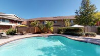 This community amenity space offers two distinct areas thoughtfully designed for recreation and wellness. The outdoor pool area serves as a centerpiece retreat, featuring a generously sized, freeform swimming pool with crystal-clear turquoise water. The surrounding deck provides ample space for lounging, complemented by shaded seating with patio umbrellas and lush tropical landscaping, including mature palm trees and manicured shrubs. The warm, open-sky setting creates a resort-like atmosphere ideal for relaxation.

Adjacent to the outdoor space is a bright, well-equipped fitness center that caters to a full range of workout needs. The interior is finished with light wood-toned flooring, neutral gray walls, and floor-to-ceiling mirrors that amplify the sense of space and light. Large sliding glass doors and windows flood the room with natural light and offer direct views of the outdoor pool area. The facility includes a comprehensive selection of cardio equipment — treadmills, ellipticals, and stationary bikes — alongside a full rack of dumbbells, cable machines, weight benches, and medicine balls. Overhead ceiling fans and recessed lighting ensure a comfortable environment, while open shelving stocked with rolled towels adds a polished, practical touch throughout the space.