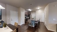 This single-floor, 2-bedroom, 2-bathroom residence features an open-concept layout that connects the kitchen and dining areas into a cohesive living space. The kitchen is equipped with stainless steel appliances, including a refrigerator, microwave, and range, complemented by dark espresso cabinetry that provides ample storage. A central kitchen island with a granite countertop and seating for multiple guests serves as both a functional workspace and a casual dining spot, with upholstered bar-height chairs adding a comfortable touch.

Dark hardwood-style flooring runs throughout the space, creating a warm, cohesive aesthetic that contrasts cleanly with the neutral-toned walls and crisp white doors and trim. The open layout allows for easy flow between the kitchen island and an adjacent dining area, making the space well-suited for entertaining. Flush-mount ceiling lighting illuminates the kitchen and main living areas effectively.

The two bedrooms are accessible via white panel doors visible in the background, offering privacy from the main living space. The overall design balances contemporary finishes with a practical, well-organized floor plan ideal for everyday living.