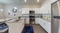 This single-story residence offers a thoughtfully designed layout that balances open communal spaces with private retreats. The living area features rich hardwood-style flooring, recessed lighting, and a sliding glass door that draws in natural light while providing outdoor access. Distinctive open shelving units add a rustic-modern character to the space.

The kitchen is well-equipped with white shaker cabinetry, granite countertops, stainless steel appliances, and pendant lighting above a breakfast bar with counter seating. Adjacent to the kitchen, the dining area accommodates a sizable table beneath a chandelier, creating a seamless flow for entertaining.

Two bedrooms provide comfortable accommodations, each with plush carpet, windows with blinds, and ample wall space for artwork. A flexible room with sliding door access serves well as a home office or additional lounge area. Both bathrooms are finished with white cabinetry, granite countertops, hardwood-style flooring, and tub-shower combinations. The primary bathroom features a double vanity for added convenience.

Neutral wall tones throughout create a cohesive, contemporary aesthetic that complements the space's functional design.