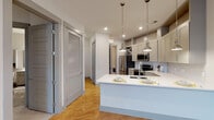 Located at 900 Hobbs Rd in Greensboro, NC, this single-floor residence offers a thoughtfully designed layout with modern finishes throughout. The open-concept kitchen is a standout feature, showcasing gray shaker-style cabinetry that extends to the ceiling, white quartz countertops, a subway tile backsplash, and stainless steel appliances including a refrigerator, range, and over-the-range microwave. A peninsula with an undermount sink and pendant lighting serves as a natural gathering point and provides additional prep and dining space. Warm hardwood-style flooring flows through the main living areas, complemented by neutral walls and recessed lighting that enhance the bright, airy feel. The living area is spacious and open, featuring a ceiling fan and glass French doors that allow natural light and provide access to an outdoor balcony. The bedroom is carpeted for comfort and includes a window with exterior views and ample wall space. The bathroom is well-appointed with a tiled tub-and-shower combination, gray vanity cabinetry, a white quartz countertop, and a wall-mounted storage cabinet. A dedicated in-unit laundry area with a full-size washer and dryer and overhead wire shelving adds practical convenience. Louvered closet doors throughout provide ample storage options.