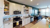 This single-floor residence offers a thoughtfully designed open-concept layout that seamlessly connects the kitchen, dining, and living areas. The kitchen is a functional centerpiece, featuring white shaker-style cabinetry extending to the ceiling, quartz countertops, a stainless steel appliance suite including a French door refrigerator with ice maker, electric range, built-in microwave, and dishwasher. A kitchen island provides additional prep space and flows naturally into the main living area, which is accented by a bold teal-green feature wall and rich wood-look flooring throughout. The living room benefits from generous natural light through large windows and a sliding glass door, offering outdoor views and balcony access. The bedroom continues the modern aesthetic with a ceiling fan, large windows, a bold accent wall, and ample natural light. The bathroom is well-equipped with a vanity featuring quartz countertops, a framed mirror, and a shower with curtain enclosure. Adjoining the bathroom is a spacious walk-in closet outfitted with wire shelving and hanging rods, providing practical storage. An additional large closet with multi-tiered wire shelving adds further storage capacity. Wood-look flooring runs consistently throughout the space, tying together a cohesive and contemporary interior design.