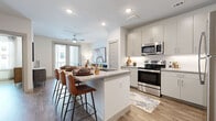 This well-designed single-floor residence offers a thoughtfully laid-out living space with contemporary finishes throughout. The open-concept kitchen is a standout feature, equipped with stainless steel appliances including a range, over-the-range microwave, and full-size refrigerator. Soft gray cabinetry is complemented by granite-style countertops and a subway tile backseat, while an island with seating provides both additional prep space and a casual dining area. Wood-look plank flooring runs seamlessly throughout the entire unit, adding warmth and visual continuity.

The living area is bright and airy, benefiting from large windows and a glass door that invites natural light and provides access to an outdoor space. The bedroom is generously sized, featuring large windows with views to the exterior, a ceiling fan, and room for substantial furnishings. It connects directly to a full bathroom outfitted with a granite-topped vanity, a glass-enclosed shower, and matching wood-look flooring. A spacious walk-in closet off the bedroom offers multi-tier shelving and hanging rods, providing ample storage. The overall ambiance is clean, modern, and move-in ready.