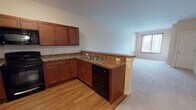 Located at 1 Overlook Dr in Monroe Township, New Jersey, this single-floor residence offers a thoughtfully designed layout with a seamless flow between the kitchen and living areas. The kitchen is a standout feature, showcasing rich cherry wood cabinetry with brushed nickel hardware, granite-style countertops, and black appliances including an electric range, over-the-range microwave, and dishwasher. A peninsula counter provides a natural transition into the open living area, which is finished with neutral-toned carpet and receives natural light through a large window. The bedroom spaces continue the warm, neutral palette with carpeted floors and multiple windows dressed with blinds, offering ample natural light and views of the surrounding greenery. A spacious walk-in closet with wire shelving provides generous storage. The bathroom is cleanly finished with tile flooring, a wood-toned vanity with a white countertop, a large mirror, and accessibility-friendly grab bars. The overall design emphasizes a clean, functional aesthetic with consistent warm tones and practical finishes carried throughout the space.