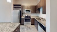 Located at 2000 Front St in Summerville, SC, this single-floor residence showcases a contemporary design with polished concrete floors that run throughout, creating a sleek and cohesive aesthetic. The open-concept layout connects the living area to the kitchen, maximizing the sense of space and encouraging effortless flow between areas.

The kitchen is well-appointed with dark wood cabinetry, granite countertops, and a full suite of stainless steel appliances including a refrigerator, electric range, microwave, and dishwasher. A built-in wine rack adds a distinctive touch, while pendant lighting overhead enhances the modern ambiance. A central island with granite surface provides additional prep space and casual seating.

The living area benefits from multiple windows that invite natural light and offer views of the surrounding exterior. Ceiling fans are installed throughout, promoting comfort year-round. A glass-paned entry door further brightens the space.

The bathroom maintains the same design language as the rest of the unit, featuring granite countertops on the vanity, a full tub-shower combination, and consistent concrete flooring. Clean lines and neutral tones throughout the space create a calm, functional environment well-suited to modern living in the heart of Summerville.