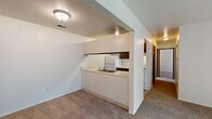 Located at 1630 Leonard St NE in Grand Rapids, Michigan, this two-bedroom, one-bathroom unit offers a functional and well-organized single-floor layout. The living area is carpeted and filled with natural light, anchored by a sliding glass door that opens onto a private wooden balcony with outdoor views of the surrounding neighborhood. The pass-through kitchen connects seamlessly to the living space, featuring dark wood cabinetry, a double-basin sink, a white refrigerator, and an electric range — providing all essential appliances in a compact, efficient arrangement. A central hallway leads to both bedrooms, each finished with neutral carpet and window blinds that allow for controlled natural light. The primary bedroom is generously sized and includes a wide walk-in closet equipped with wire shelving and a full-length hanging rod for ample storage. The second bedroom is more intimate, also featuring a window with blinds and neutral finishes throughout. The full bathroom includes a shower-tub combination, a single vanity with a wood-toned cabinet, tile flooring, and a well-lit mirror. Neutral wall tones and consistent carpeting throughout the unit create a cohesive, move-in-ready atmosphere suited for comfortable everyday living.