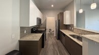 This 670-square-foot, single-story apartment located on E Apache Blvd in Tempe, AZ, offers a practical and modern layout across 2 bedrooms and 2 bathrooms. The galley-style kitchen is well-appointed with granite countertops, dark wood lower cabinets, crisp white upper cabinets, a tile backsplash, wood-look vinyl flooring, and stainless steel appliances including a refrigerator, range, microwave, and dishwasher. The primary bedroom spans 140 square feet and features plush carpeting, a ceiling fan, two windows with horizontal blinds offering urban views of surrounding buildings, and a walk-in closet. The second bedroom also features carpet flooring, a window with blinds, and ample wall space. Both bathrooms are finished with floor-to-ceiling rectangular tile surrounds in a neutral taupe tone. One bathroom includes a walk-in shower with a white basin, while the second features a full soaking tub with a curved chrome curtain rod. Neutral gray walls and white trim carry throughout the unit, creating a clean, cohesive aesthetic. The overall ambiance is modern and move-in ready, well-suited for urban living in the heart of Tempe.