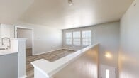 This single-story home offers a thoughtfully organized layout encompassing three bedrooms, two bathrooms, a kitchen, a dedicated laundry room, and two closets. The living area features light wood-tone flooring and neutral gray walls, with a bank of windows fitted with white blinds that allow ample natural light to fill the space. A half-wall divider adds architectural interest while maintaining an open feel between areas.

The kitchen is equipped with white cabinetry, light countertops, a subway tile backsplash, and black appliances including a range, over-the-range microwave, and refrigerator. Light hardwood-style flooring carries throughout the kitchen and connects seamlessly to adjacent spaces.

The bedrooms feature plush carpet and windows with blinds. The primary bedroom is a comfortable size and is served by closet storage. One bedroom includes a ceiling fan with light fixture, while another features an electrical panel access point. The bathrooms are finished with white cabinetry, light countertops, and a tub-shower combination with chrome fixtures and light wood-style flooring. The laundry room includes upper cabinetry and washer/dryer hookups, providing practical utility storage.