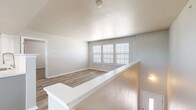 This single-story home offers a thoughtfully organized layout encompassing three bedrooms, two bathrooms, a kitchen, a dedicated laundry room, and two closets. The living area features light wood-tone flooring and neutral gray walls, with a bank of windows fitted with white blinds that allow ample natural light to fill the space. A half-wall divider adds architectural interest while maintaining an open feel between areas.

The kitchen is equipped with white cabinetry, light countertops, a subway tile backsplash, and black appliances including a range, over-the-range microwave, and refrigerator. Light hardwood-style flooring carries throughout the kitchen and connects seamlessly to adjacent spaces.

The bedrooms feature plush carpet and windows with blinds. The primary bedroom is a comfortable size and is served by closet storage. One bedroom includes a ceiling fan with light fixture, while another features an electrical panel access point. The bathrooms are finished with white cabinetry, light countertops, and a tub-shower combination with chrome fixtures and light wood-style flooring. The laundry room includes upper cabinetry and washer/dryer hookups, providing practical utility storage.