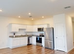 This 1,290 sq ft two-story home in Ruskin, FL offers 3 bedrooms, 3 bathrooms, and a well-organized layout across two floors. The ground floor (540 sq ft) features an open-concept kitchen and living room with wood-look luxury vinyl plank flooring throughout. The kitchen is equipped with stainless steel appliances, including a refrigerator, electric range, and over-the-range microwave, complemented by white cabinetry and granite-look countertops. The living room opens directly to the backyard via sliding glass doors, allowing natural light to fill the space. A half bathroom on the main floor features a pedestal sink, round mirror, and wood-look flooring. The attached garage includes an automatic opener and houses the home's electrical panel. The upper floor (750 sq ft) holds all three bedrooms, each with carpet flooring and ample natural light from windows with views of the surrounding greenery. The primary bedroom spans 210 sq ft and includes a spacious walk-in closet with wire shelving systems on two walls. Additional bedrooms feature closets and are served by the remaining full bathrooms. Three hallways connect the rooms efficiently across both levels, and three closets provide generous storage throughout the home.